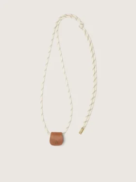 Estuche para lentes con una correa tipo senderismo de color crema y un clip de cuero color canela