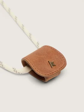 Estuche para lentes con una correa tipo senderismo de color crema y un clip de cuero color canela